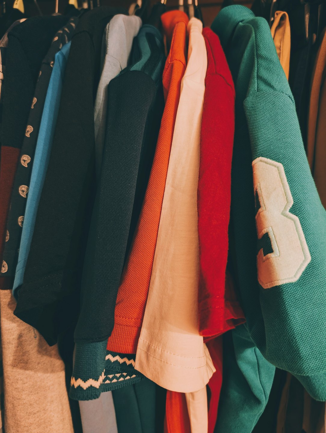 Colorful shirts and sweaters hanging on a clothing rack.